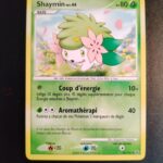 Shaymin 38/127. Carte du JCC Pokémon issue de la série Platine du bloc Platine, parue le 18/08/2009. Carte Pokémon de Base de type Plante, Rare. Illustrateur: Kagemaru Himeno. L'illustration représente un petit quadrupède blanc avec une crinière verte décorées de 2 grosses fleurs roses de part et d'autre de sa tête. La créature est représentée en train de courir dans une prairie fleurie bordée de montagnes.