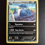 Corboss 52/119. Carte du TCG Pokémon issue de la série Vigueur Spectrale du bloc XY (XY04, XY: Vigueur Spectrale), parue le 08/11/2014. Carte Pokémon Niveau 1 de type Ténèbres, évolution de Cornèbre, Rare. Hajime Kusajima. L'illustration représente un volatile casqué perché sur le pignon d'un bâtiment ancien.