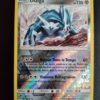 Dialga (reverse) 127/214. Carte du TCG Pokémon issue de la série Tonnerre Perdu du bloc Soleil et Lune (SL08, SL: Tonnerre Perdu), parue le 02/11/2018. Carte Pokémon de Base de type Métal. Rare. Illustrateur: nagimiso. L'illustration représente une créature monstrueuse blanche et bleue sur un terrain rocailleux, faisant face à de fortes rafales de vent.