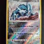 Dialga (reverse) 127/214. Carte du TCG Pokémon issue de la série Tonnerre Perdu du bloc Soleil et Lune (SL08, SL: Tonnerre Perdu), parue le 02/11/2018. Carte Pokémon de Base de type Métal. Rare. Illustrateur: nagimiso. L'illustration représente une créature monstrueuse blanche et bleue sur un terrain rocailleux, faisant face à de fortes rafales de vent.